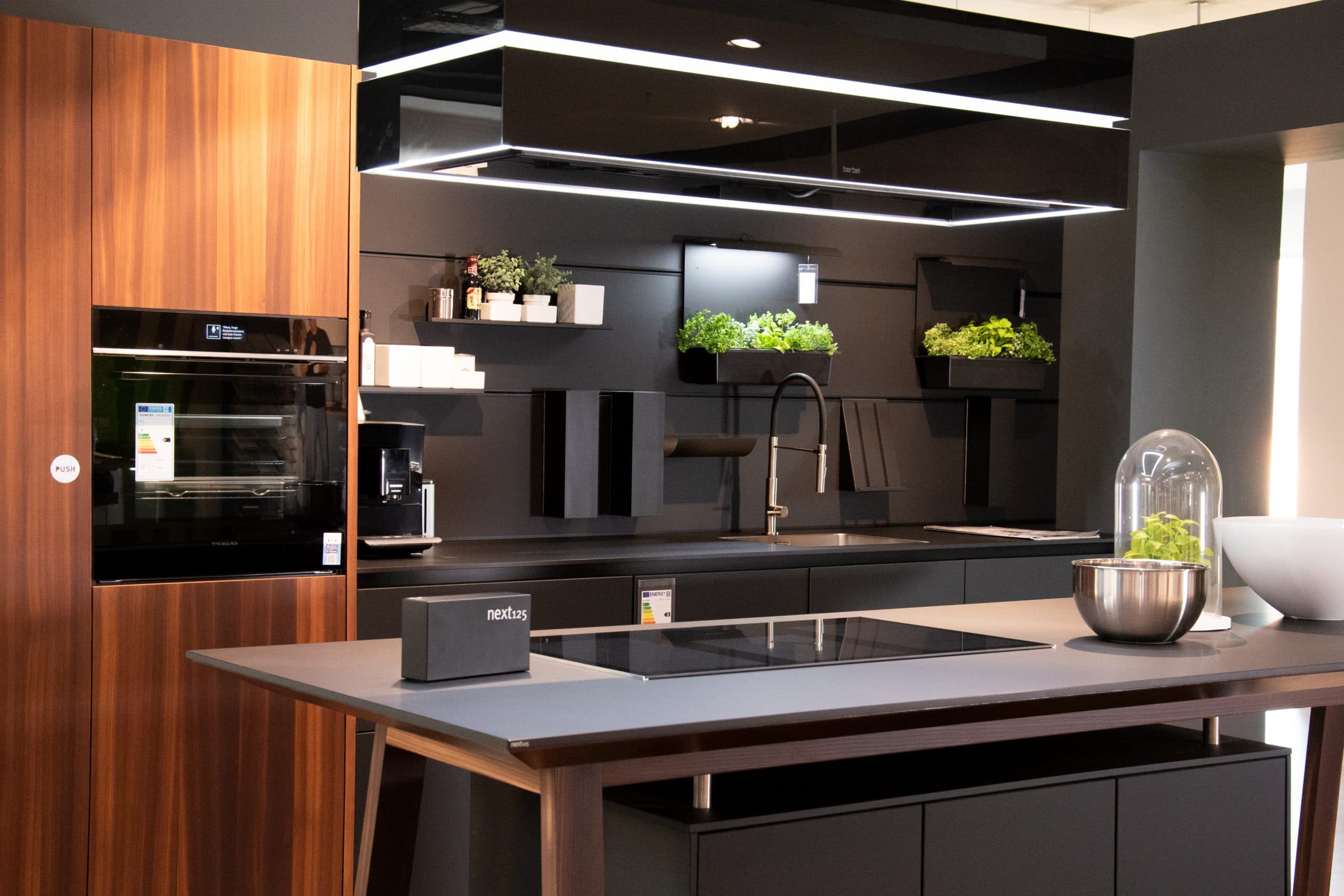 Elegante Einbauküche: NX 870 Front in Onyxschwarz feinmatt, harmonisch kombiniert mit Lärche geräuchert. Diese Küche vereint modernes Design mit natürlicher Wärme. Mit individuellen Anpassungsmöglichkeiten an Ihre Räumlichkeiten wird diese Küche zum Herzstück Ihres Zuhauses. Entdecken Sie zeitlose Schönheit und Funktionalität in einer Einbauküche, die Ihre Bedürfnisse erfüllt.
