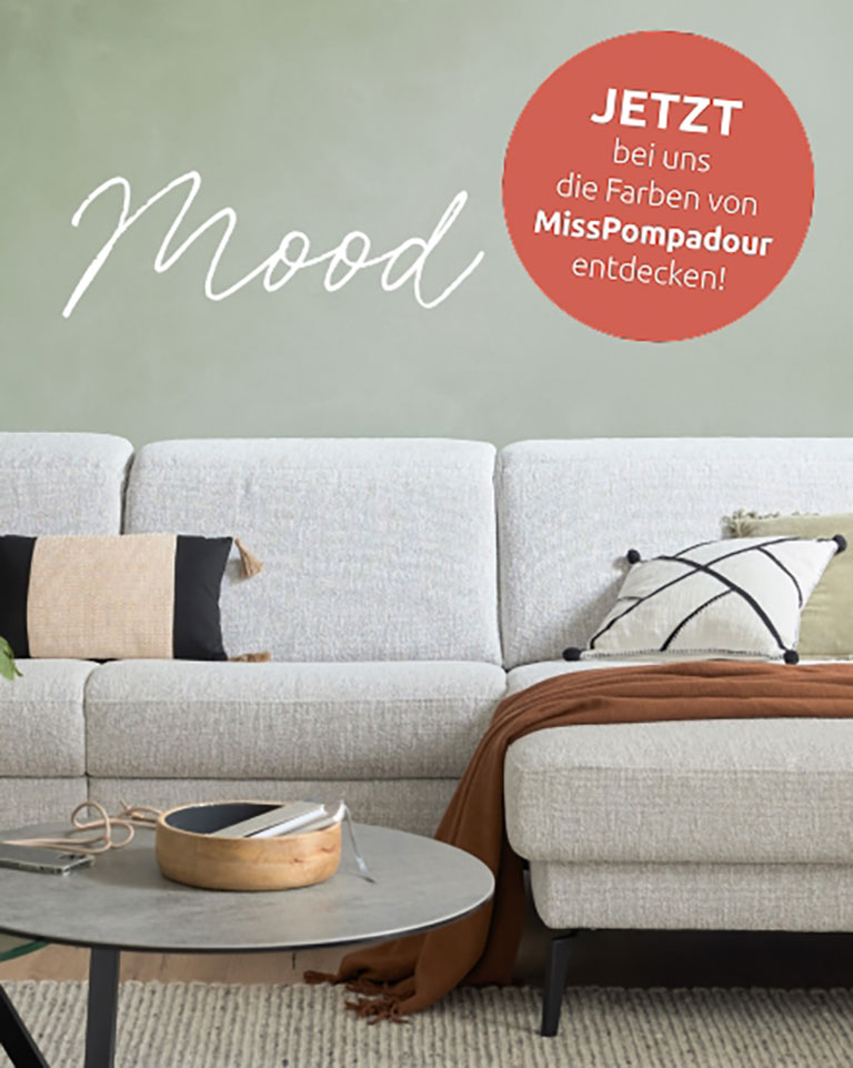 Ein modernes hellgraues Sofa mit stilvollen Kissen, ein runder Couchtisch und Mood auf einer grünen Wand.