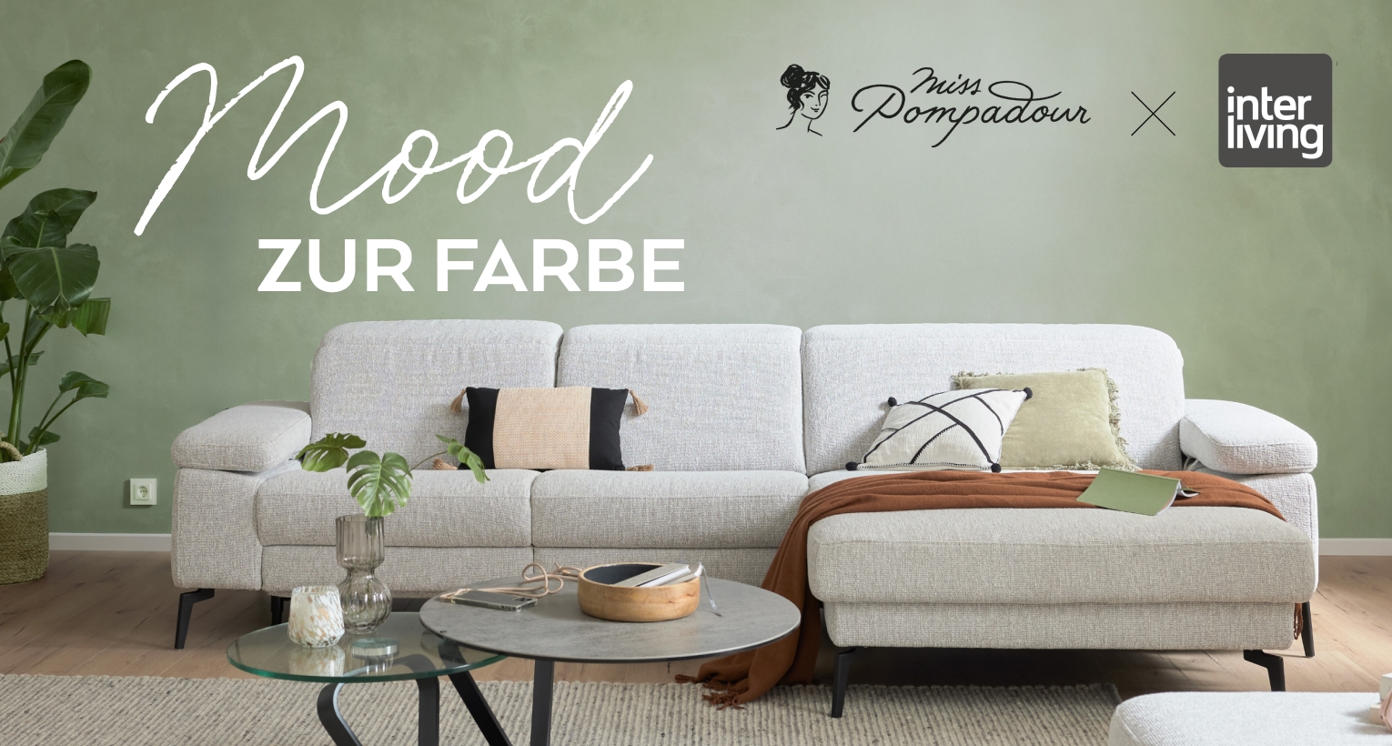 Modernes Wohnzimmer mit hellgrauem Sofa, grüner Wand, Pflanzen und stilvollem Dekor; Text: Mood zur Farbe.