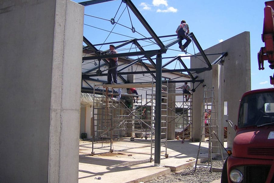 Bauarbeiter montieren auf einer Baustelle unter blauem Himmel mit Hilfe von Gerüsten und Leitern einen Metalldachstuhl.