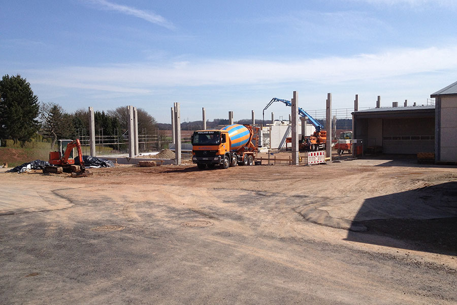 Eine Baustelle mit einem Zementmischer, einem Bagger und Gebäudesäulen unter freiem Himmel.