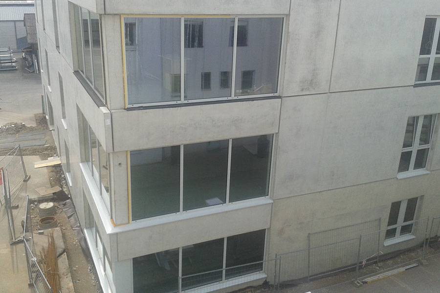 Ein modernes, unfertiges Gebäude mit großen Glasfenstern und Betonwänden, von außen gesehen während der Bauarbeiten.