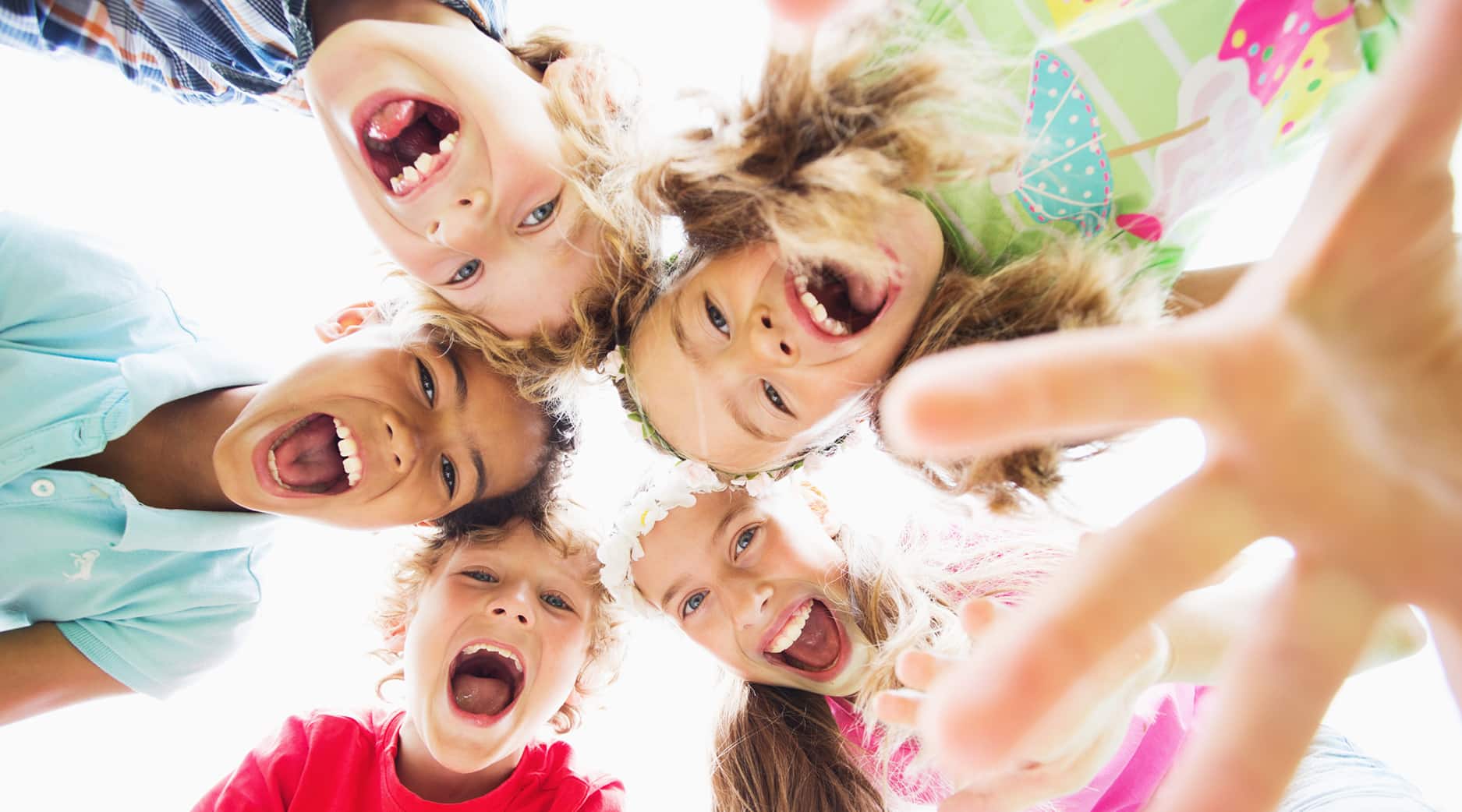 Fünf glückliche Kinder sitzen im Kreis, lächeln und lachen und schauen in die Kamera.