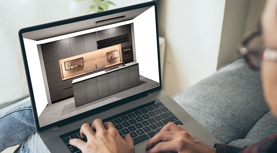 Eine Person betrachtet ein modernes Küchendesign auf einem Laptop-Bildschirm, während sie auf einer Couch sitzt.