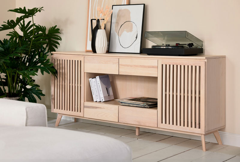 Sideboard aus hellem Holz mit Dekoration, Büchern und einem Plattenspieler, neben einer großen Grünpflanze in einem modernen Wohnzimmer.