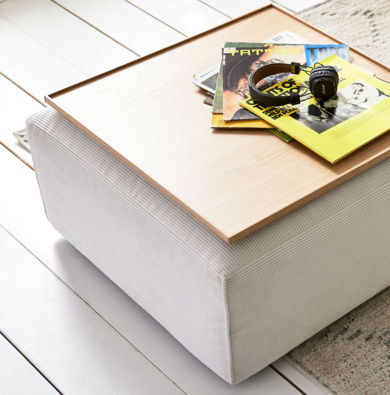 Ein Stapel Zeitschriften, Kopfhörer und eine Uhr liegen auf einem Holztablett auf einem hellen Hocker.
