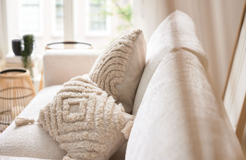 Cremefarbene, strukturierte Kissen auf einem hellen Sofa in einem hellen, gemütlichen Wohnzimmer mit weichem Tageslicht.