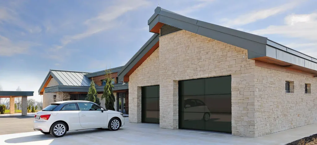 Modernes Haus mit Steinfassade, Metalldach, großen Garagentoren aus Glas und einem weißen Auto in der Einfahrt.