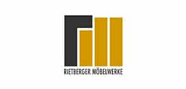 Logo mit drei senkrechten goldenen Balken und einem schwarzen Balken. Der Text darunter lautet RIETBERGER MÖBELWERKE.
