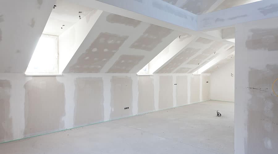 Ein großer, unausgebauter Dachboden mit Trockenbau und mehreren schrägen Fenstern, die natürliches Licht hereinlassen.