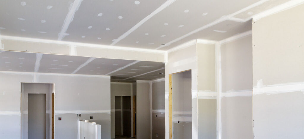 Unfertiger Raum mit neu installierter Trockenbauwand, abgeklebten Nähten und Flecken von Fugenmasse an Wänden und Decke.