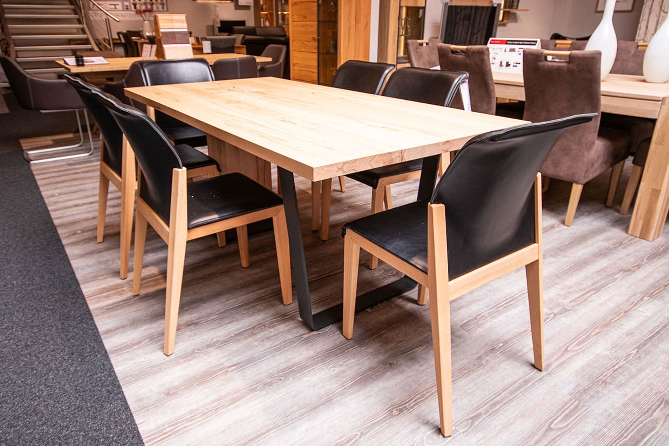 Die Tischgruppe Talis ist ein Esstisch aus Holz mit sechs Stühlen in Schwarz und Holz in einem modernen Showroom.