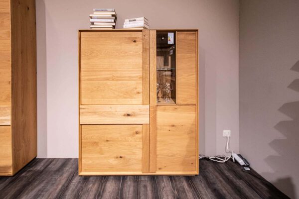 Highboard Woodline mit gestapelten Büchern darauf, Gläsern darin und Stromkabeln daneben auf dem Boden.