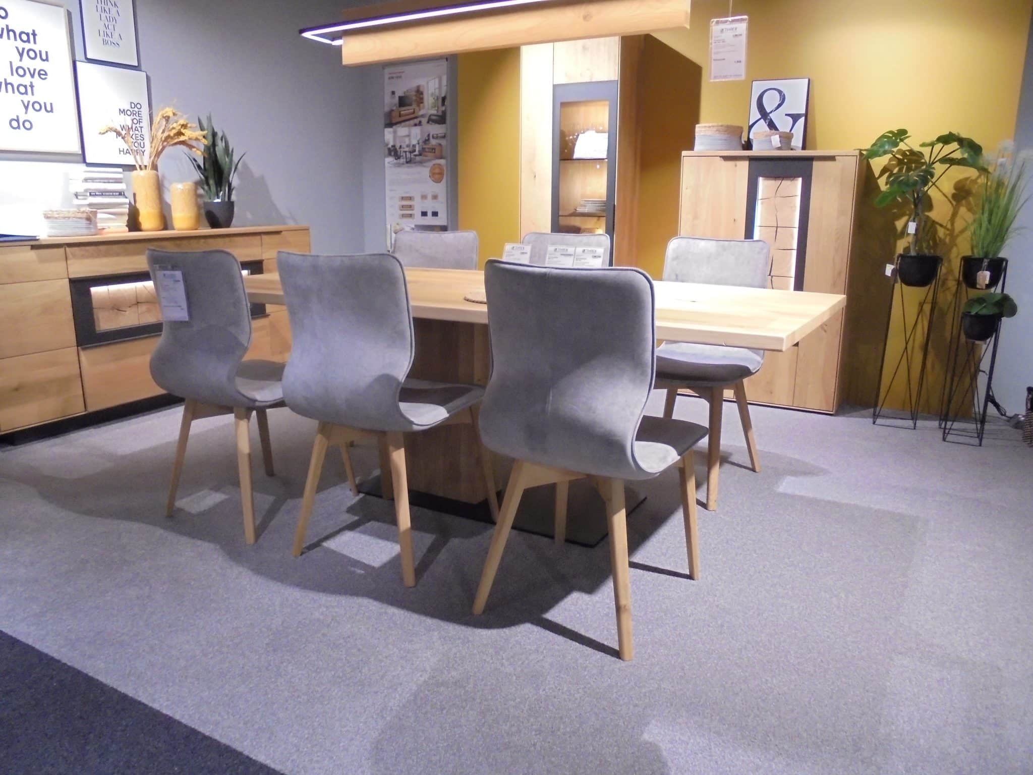 Modernes Esszimmer mit der Tischgruppe WM1910/Luna mit sechs grauen Stühlen und Holztisch vor gelb-grauen Wänden.