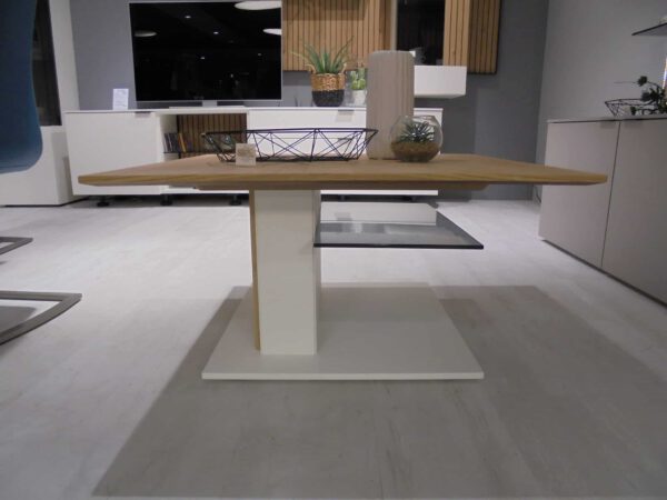 Couchtisch CT332-85: Moderner Holztisch mit weißem Sockel, Pflanzen und Metallkorb in einem minimalistischen Raum.