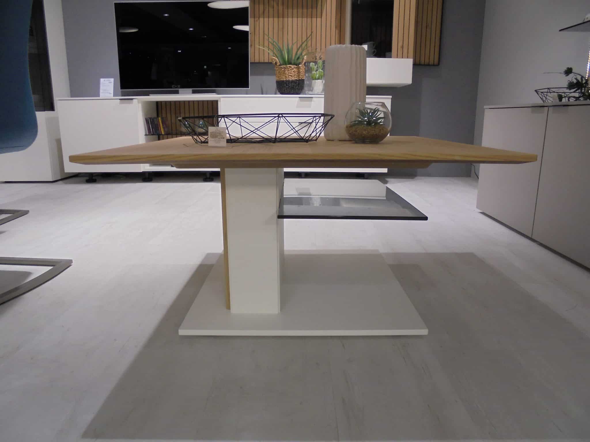 Couchtisch CT332-85: Moderner Holztisch mit weißem Sockel, Pflanzen und Metallkorb in einem minimalistischen Raum.