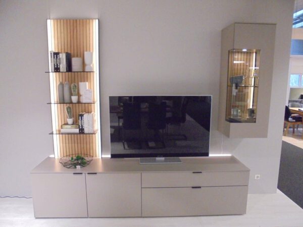 Wohnprogramm Linera: Modernes Wohnzimmer mit TV auf beigem Schrank, offenen Regalen und Glasvitrine an der Wand.