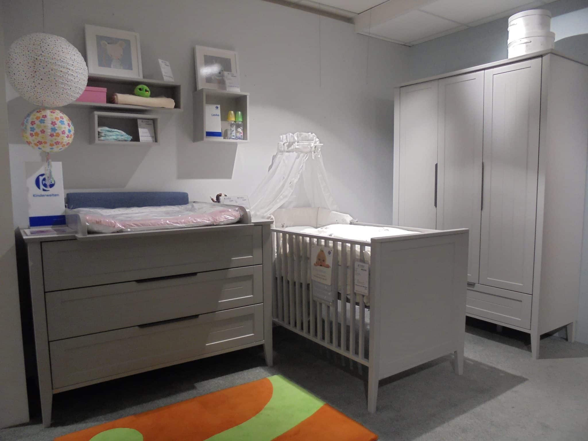 Babyzimmer Levke: modernes Kinderzimmer mit grauer Kommode, Himmelbettchen, Kleiderschrank, Regalen und buntem Teppich.