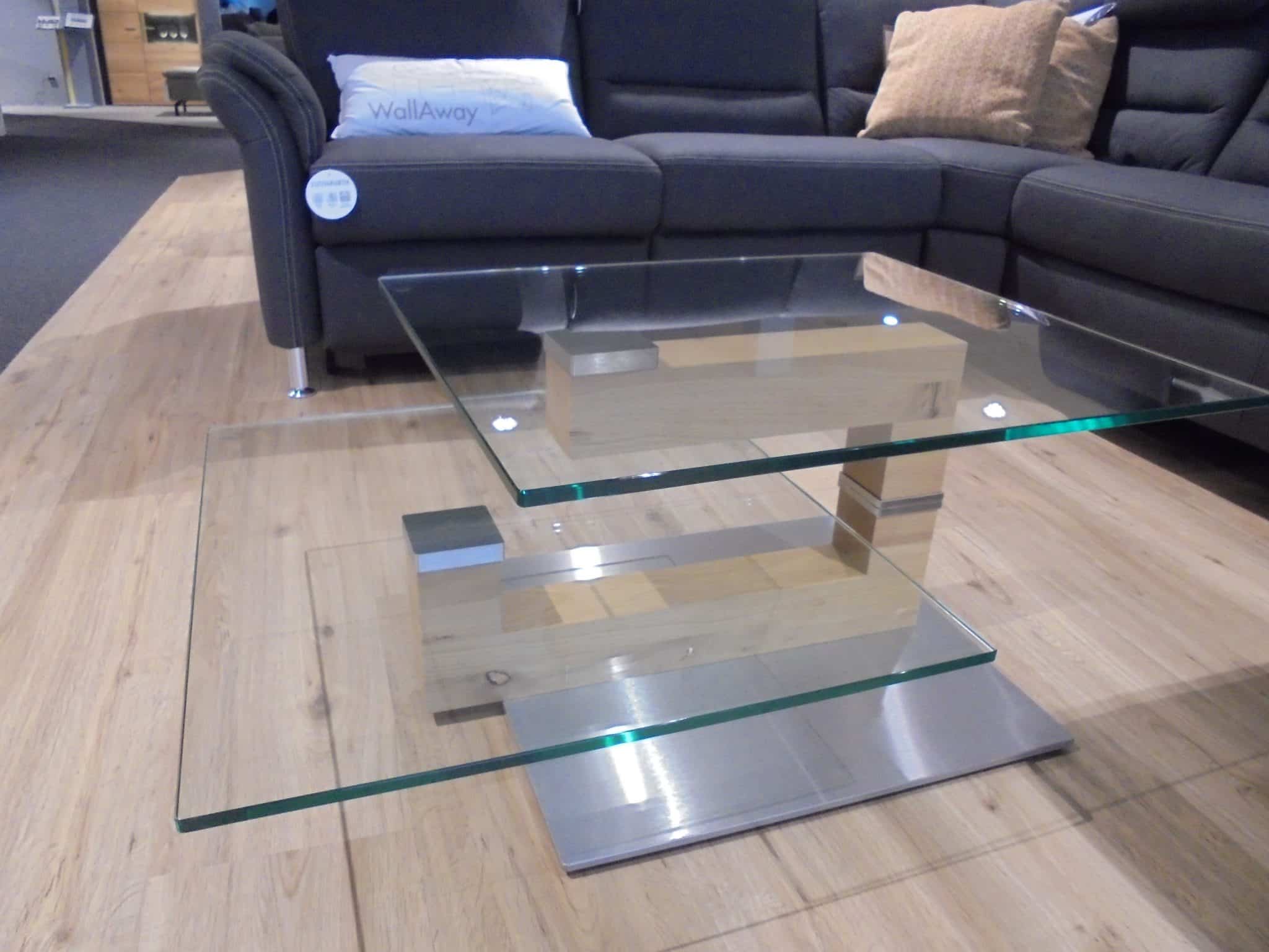 Couchtisch 4340, ein moderner Couchtisch aus Glas mit zwei Ebenen und Chromakzenten, neben einem grauen Sektionssofa.