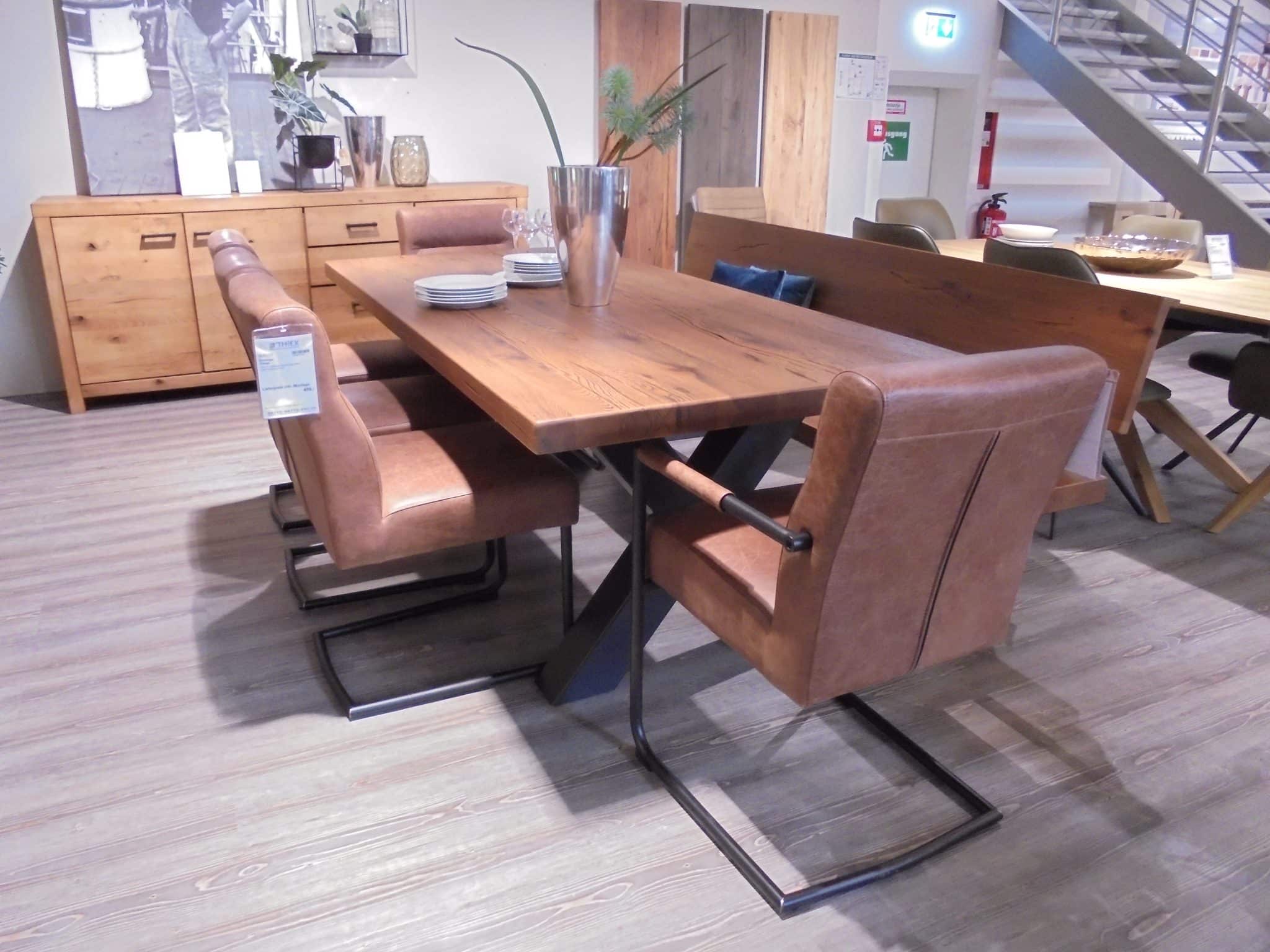 Die Tischgruppe Vintage: ein Esstisch aus Holz mit vier braunen Lederstühlen in einem modernen, hellen Ausstellungsraum.