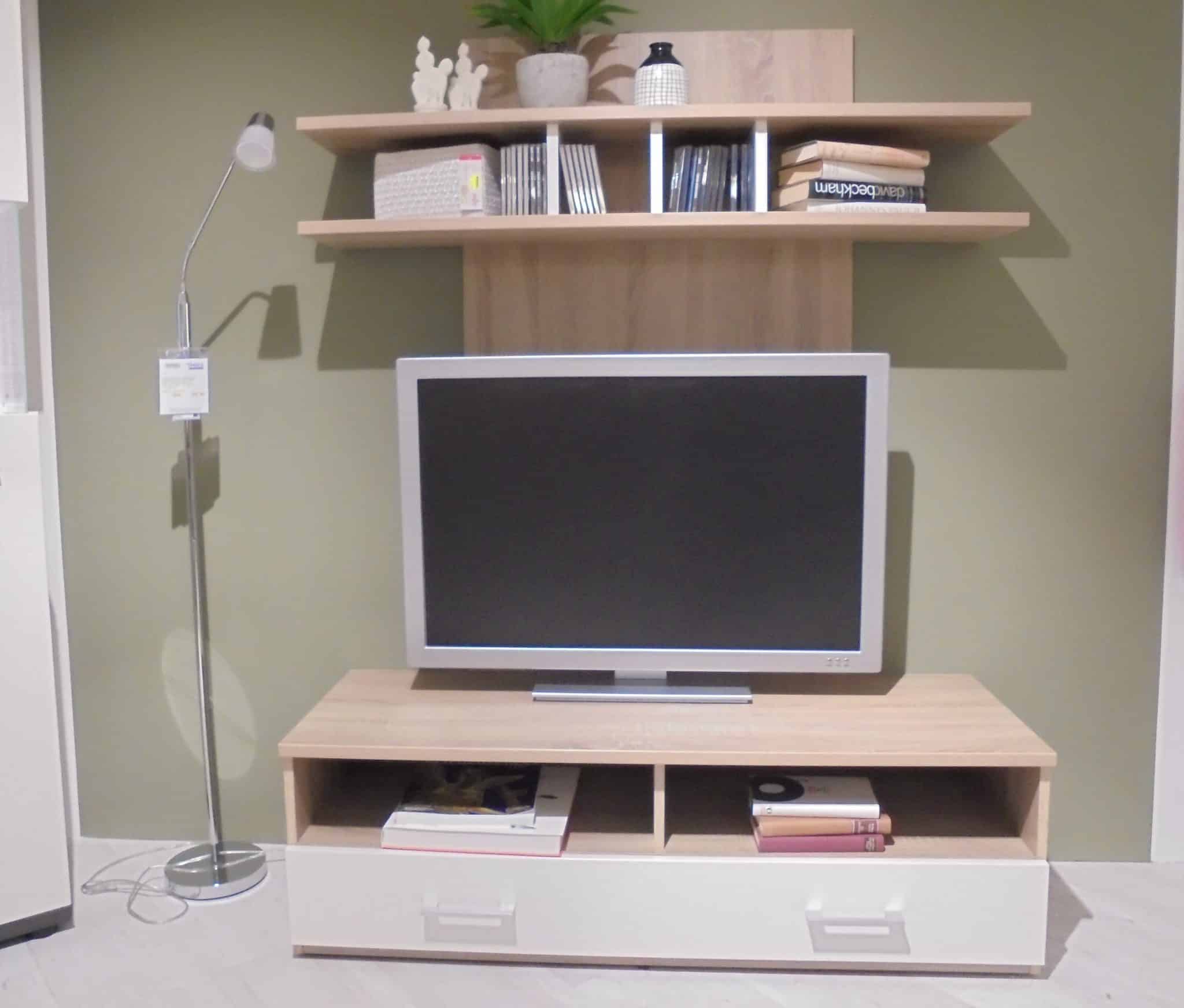 Das Medienelement Smash besteht aus einem Fernseher auf einem Holzständer mit Regalen darüber, Büchern, Dekoration und einer Stehlampe auf der linken Seite.