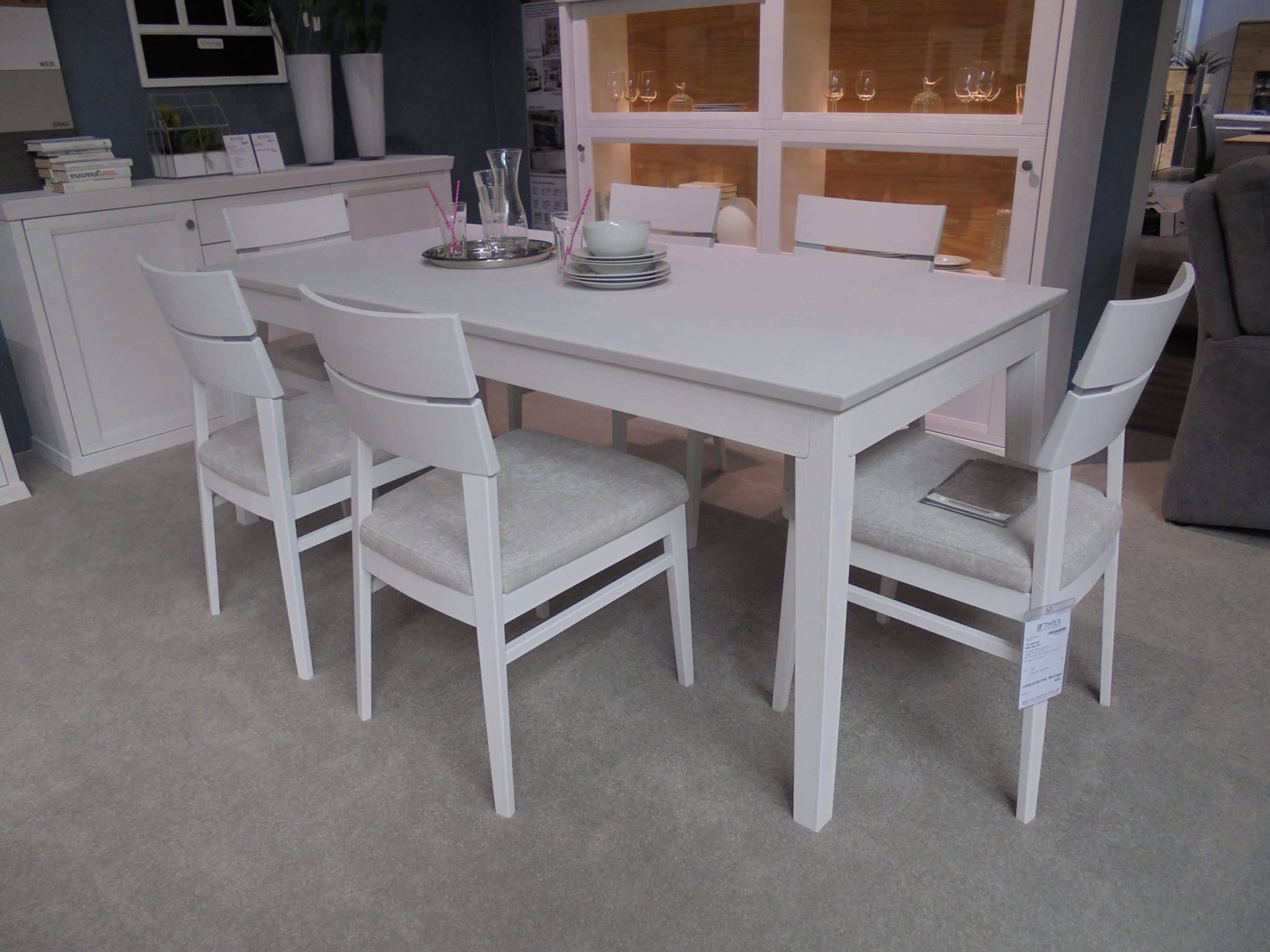 Ein modernes Esszimmer mit der Tischgruppe WM Casa 220, einem weißen rechteckigen Tisch mit vier weißen Stühlen auf einem hellen Teppich.