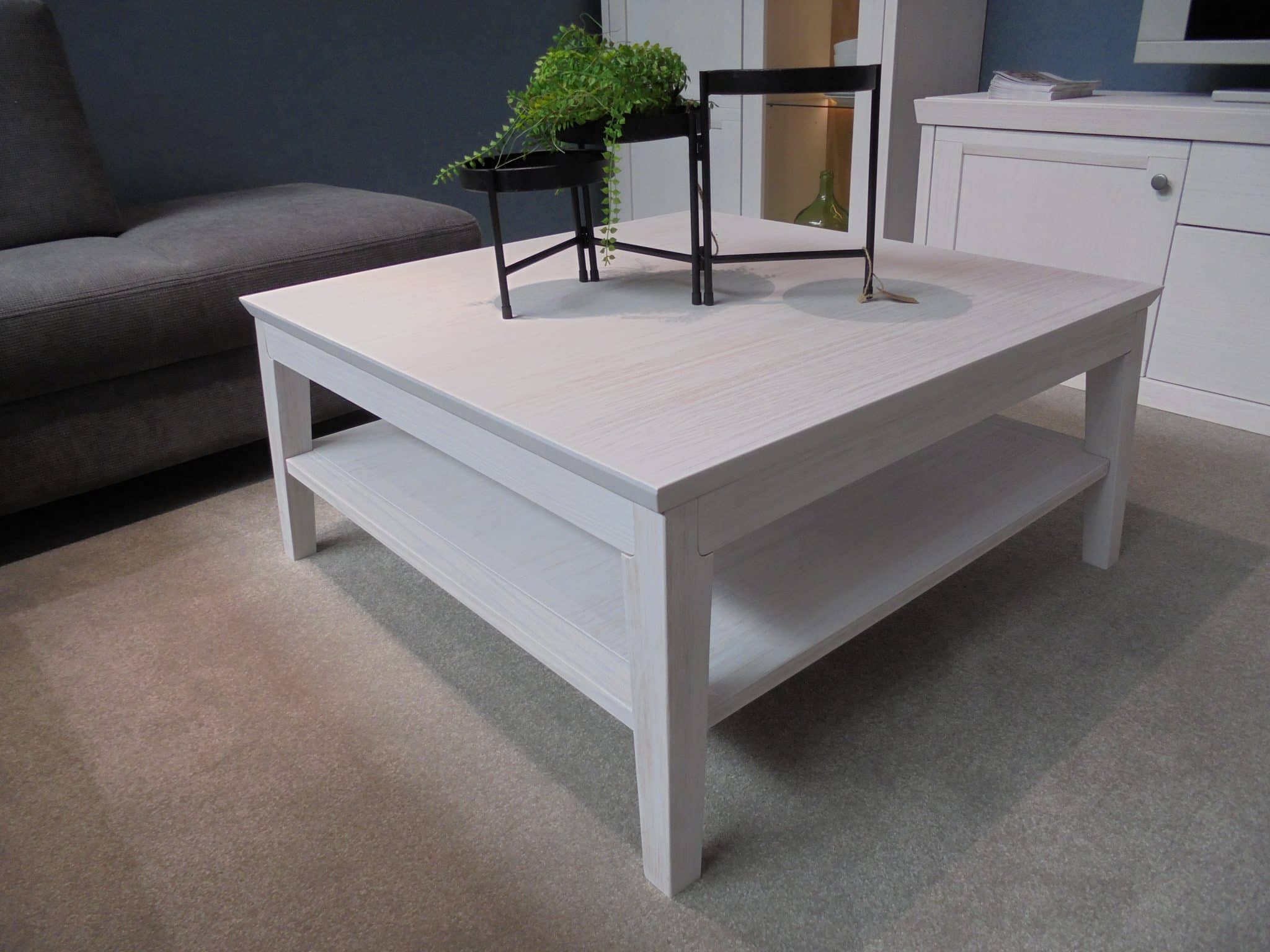 Couchtisch WM Casa 220, ein weißer quadratischer Couchtisch mit unterer Ablage, ausgestellt in einem modernen Wohnzimmer.