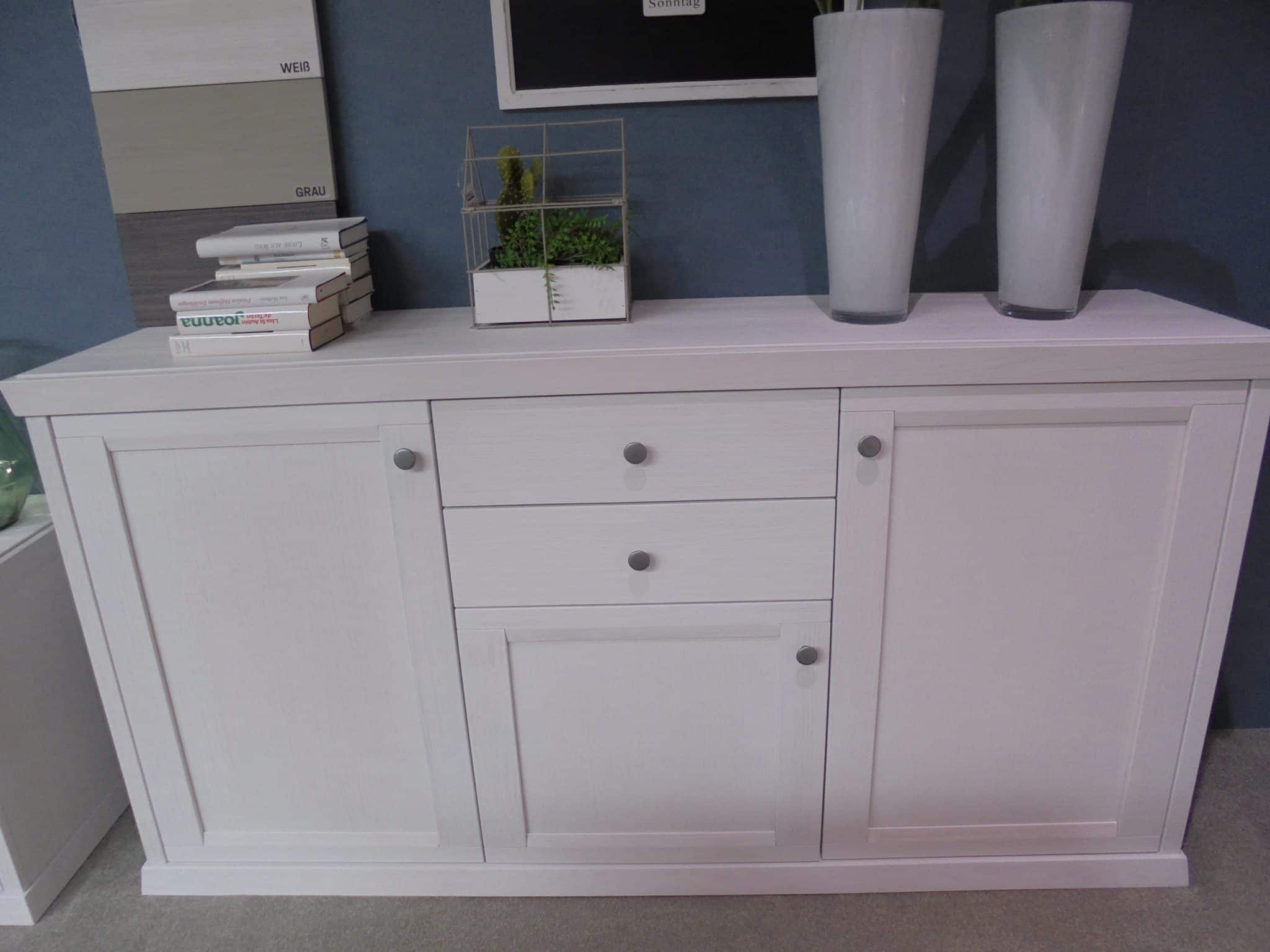 Das Sideboard WM Casa 220 verfügt über zwei Schubladen, zwei Schränke und ist mit Büchern, hohen Vasen und einer kleinen Pflanze bestückt.