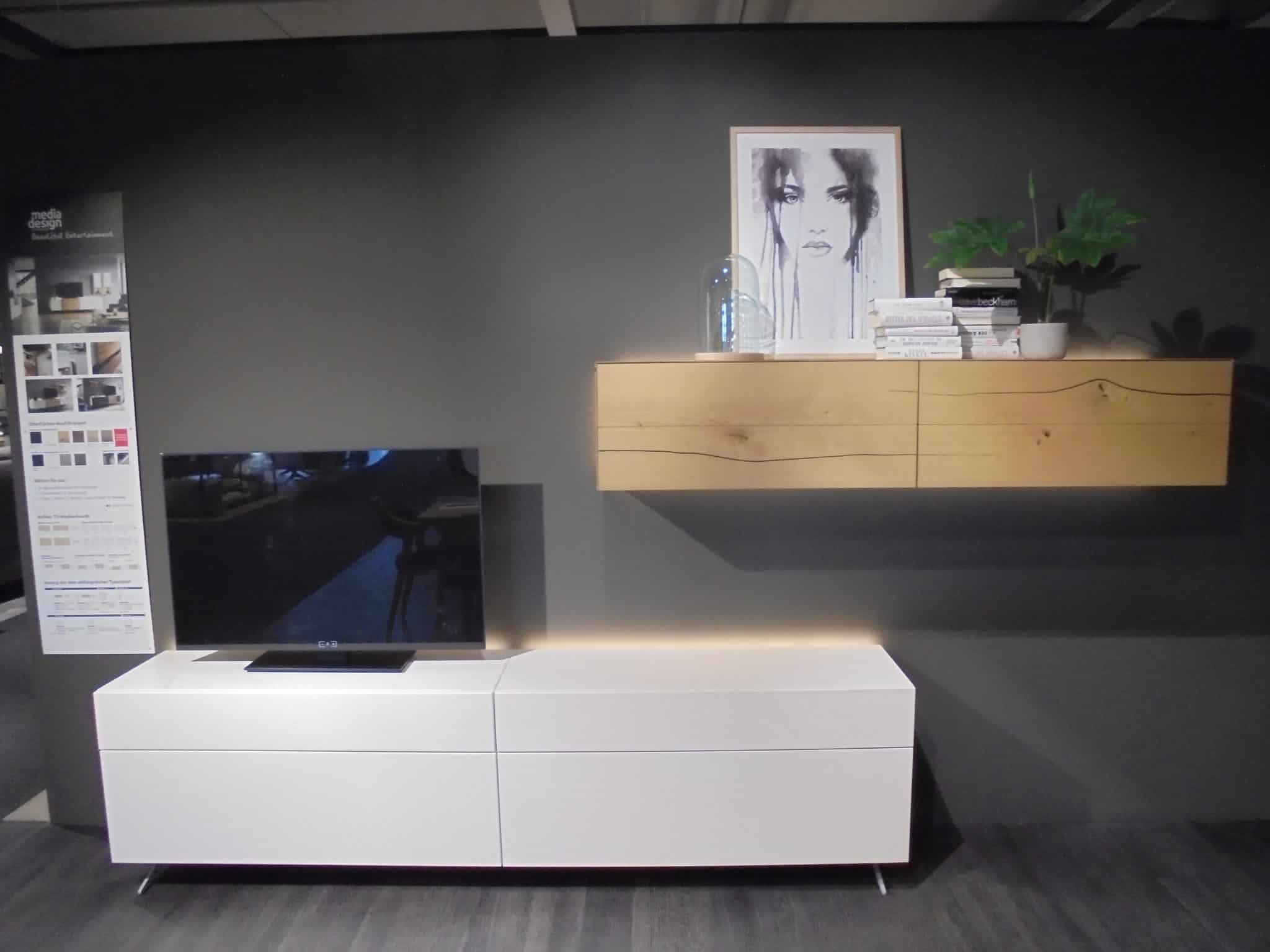 Wohnprogramm Media Design: modernes Wohnzimmer mit weißem TV-Ständer, Wandregal und gerahmter Kunst an einer dunklen Wand.