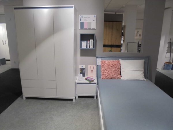 Ein modernes Schlafzimmer mit dem Jugendzimmer Home Base Set: weißer Kleiderschrank, Nachttisch, Regale und ein Bett mit blauen Betten.