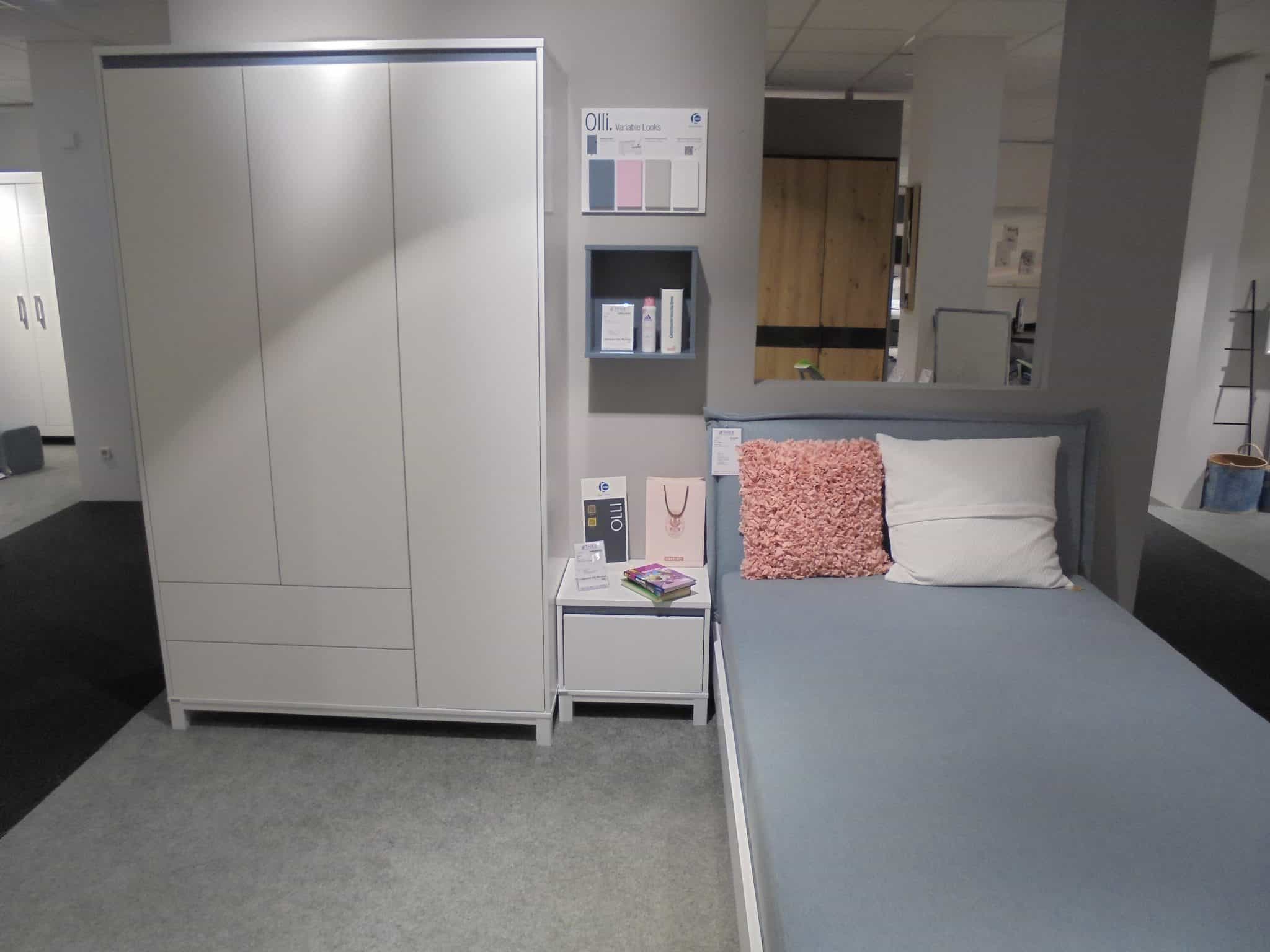 Ein modernes Schlafzimmer mit dem Jugendzimmer Home Base Set: weißer Kleiderschrank, Nachttisch, Regale und ein Bett mit blauen Betten.