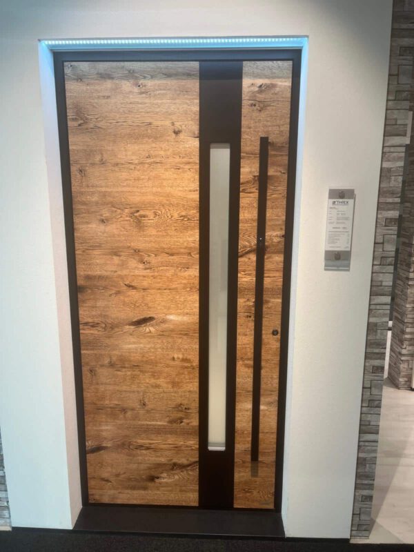 Eine moderne Holztür mit einer vertikalen Glasscheibe und einem Metallgriff, eingefasst in eine weiße Wand mit einem Etikett an der Seite.
