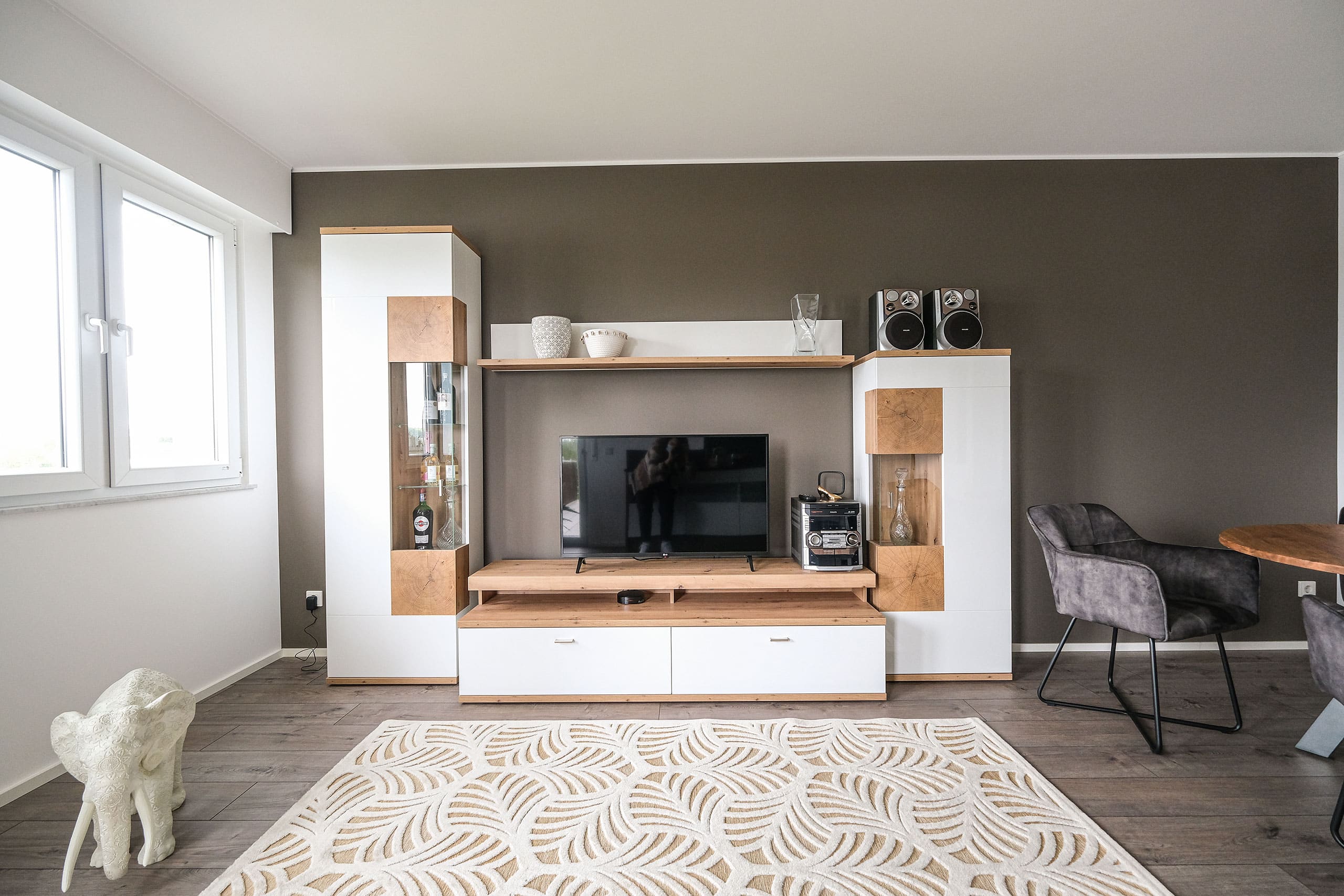 Modernes Wohnzimmer mit Fernseher, Regalen, Dekoration, Elefanten-Skulptur und gemustertem Teppich auf Holzboden.