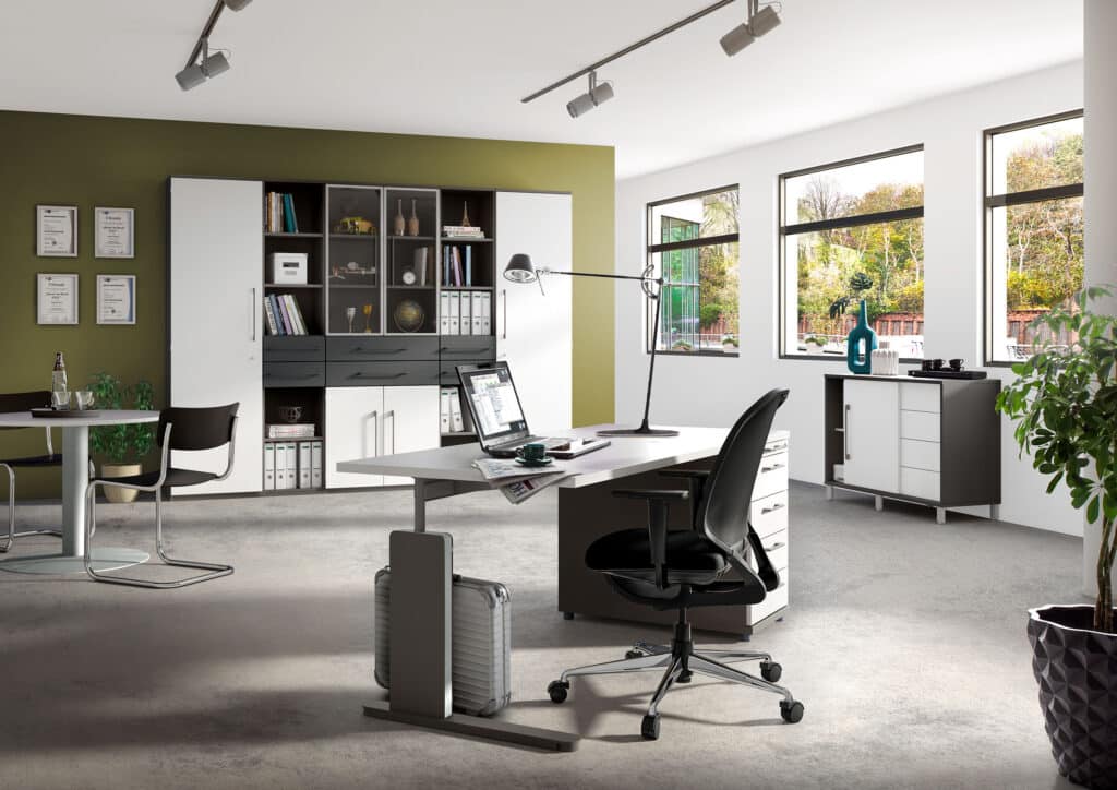 Modernes Büro mit Schreibtisch, Stuhl, Regalen und großen Fenstern, die natürliches Licht hereinlassen; Pflanzen und Dekoration sichtbar.