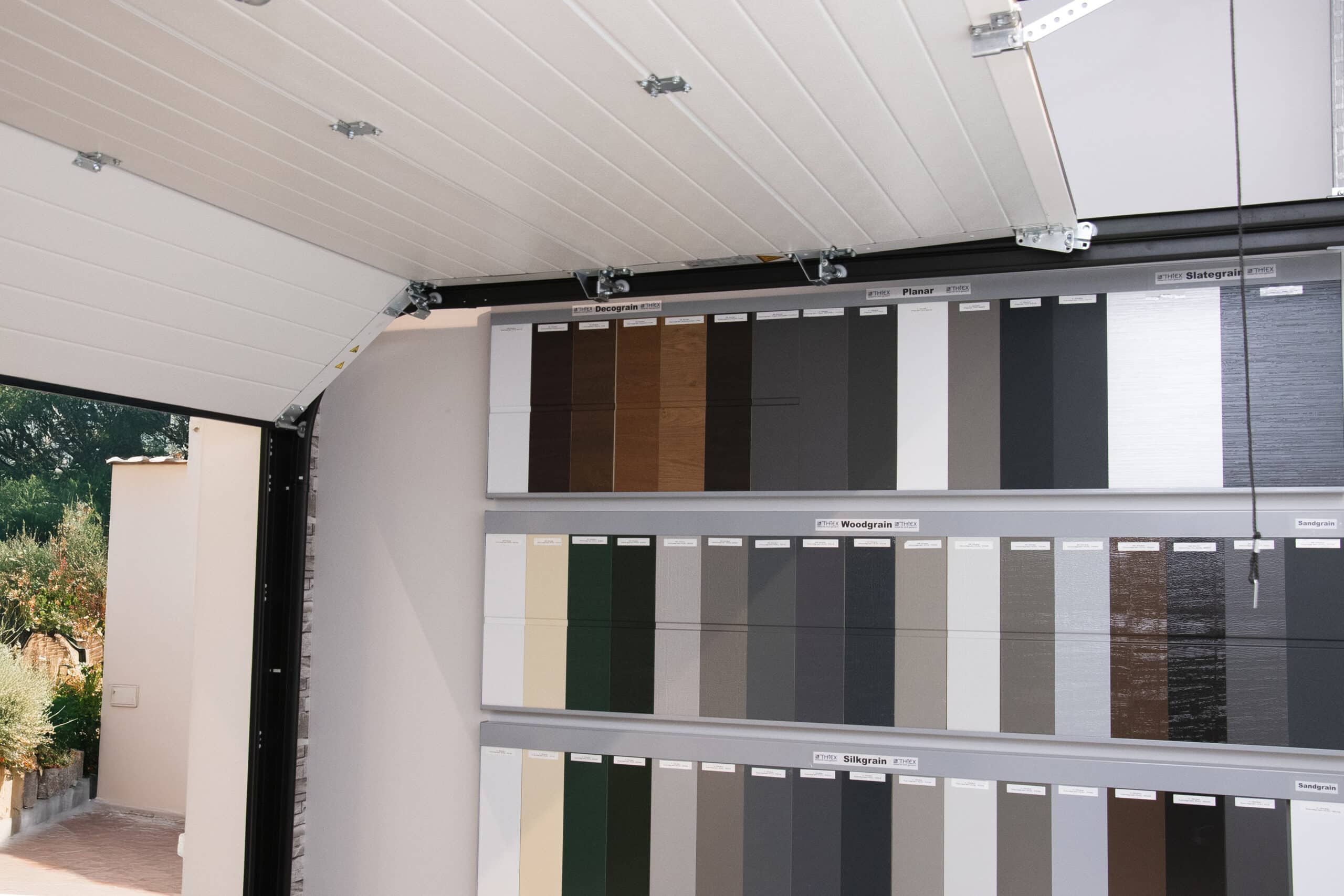 Musterplatten in verschiedenen Farben und Ausführungen sind an einer Wand innerhalb eines offenen Garagentors ausgestellt.