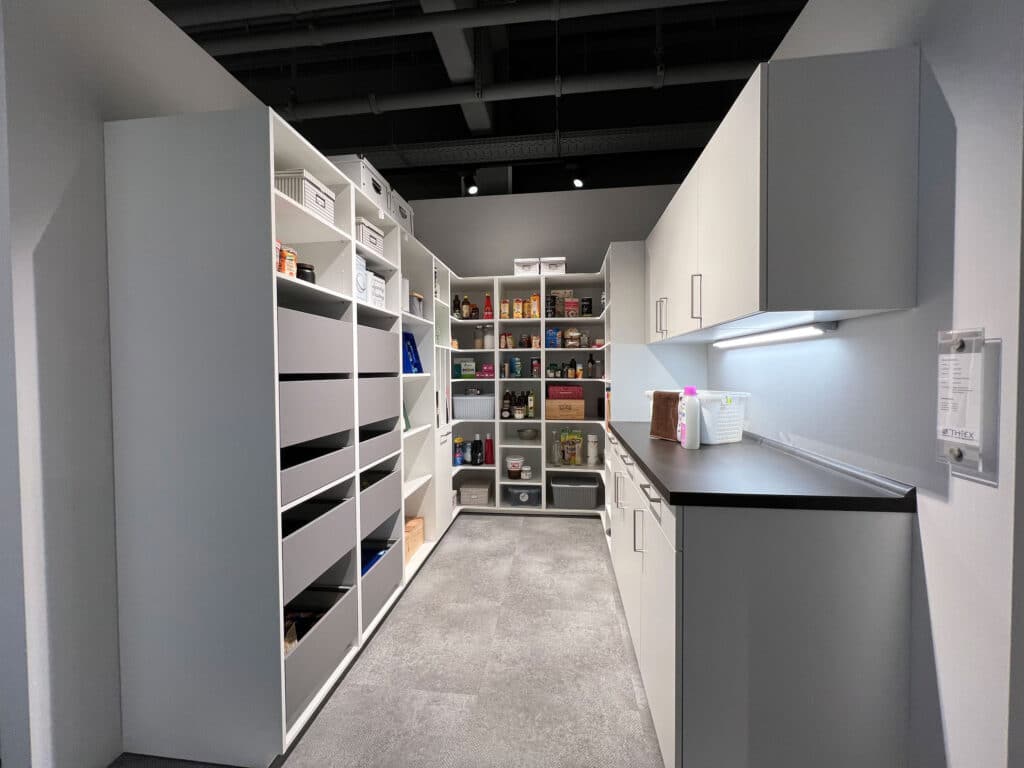 Moderne Speisekammer mit weißen Regalen, Schränken und geordneten Aufbewahrungsbehältern, mit heller Ober- und Unterschrankbeleuchtung.