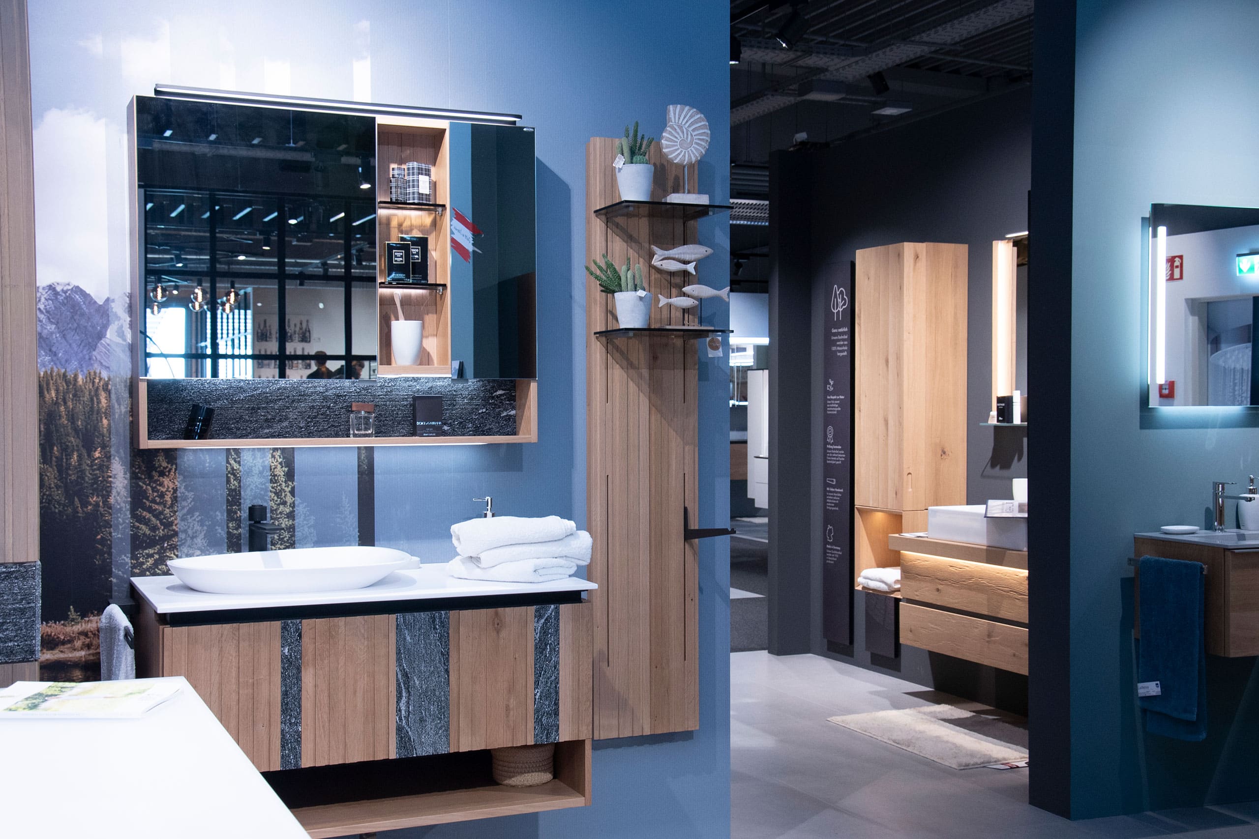 Moderner Badezimmer-Showroom mit Waschbecken aus Holz und Stein, Gefäßwaschbecken, Spiegelschrank, offenen Regalen und gefalteten Handtüchern.