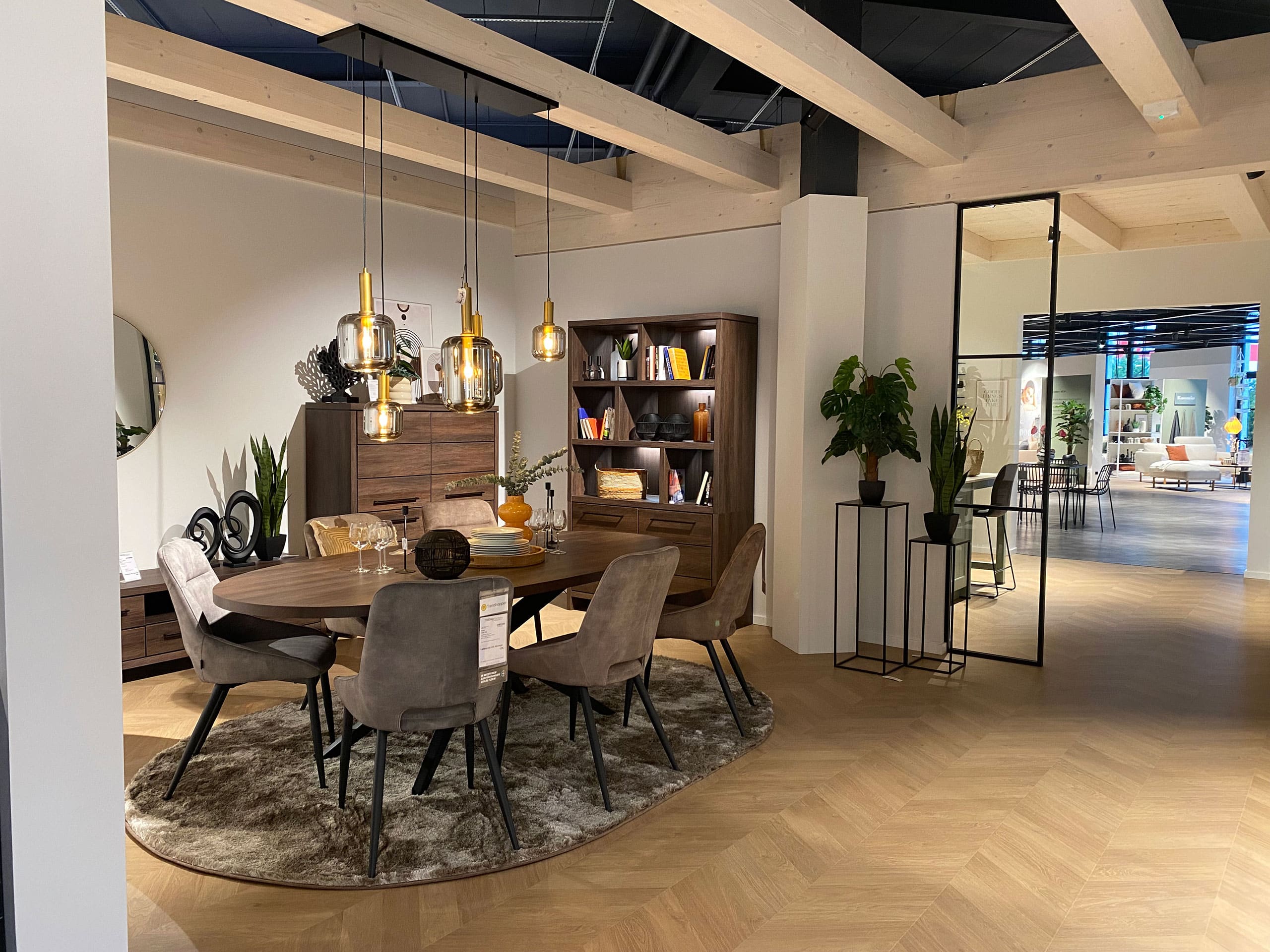 Modernes Esszimmer mit rundem Tisch, sechs Stühlen, Hängelampen, Bücherregal und Dekoration auf einem Holzboden.