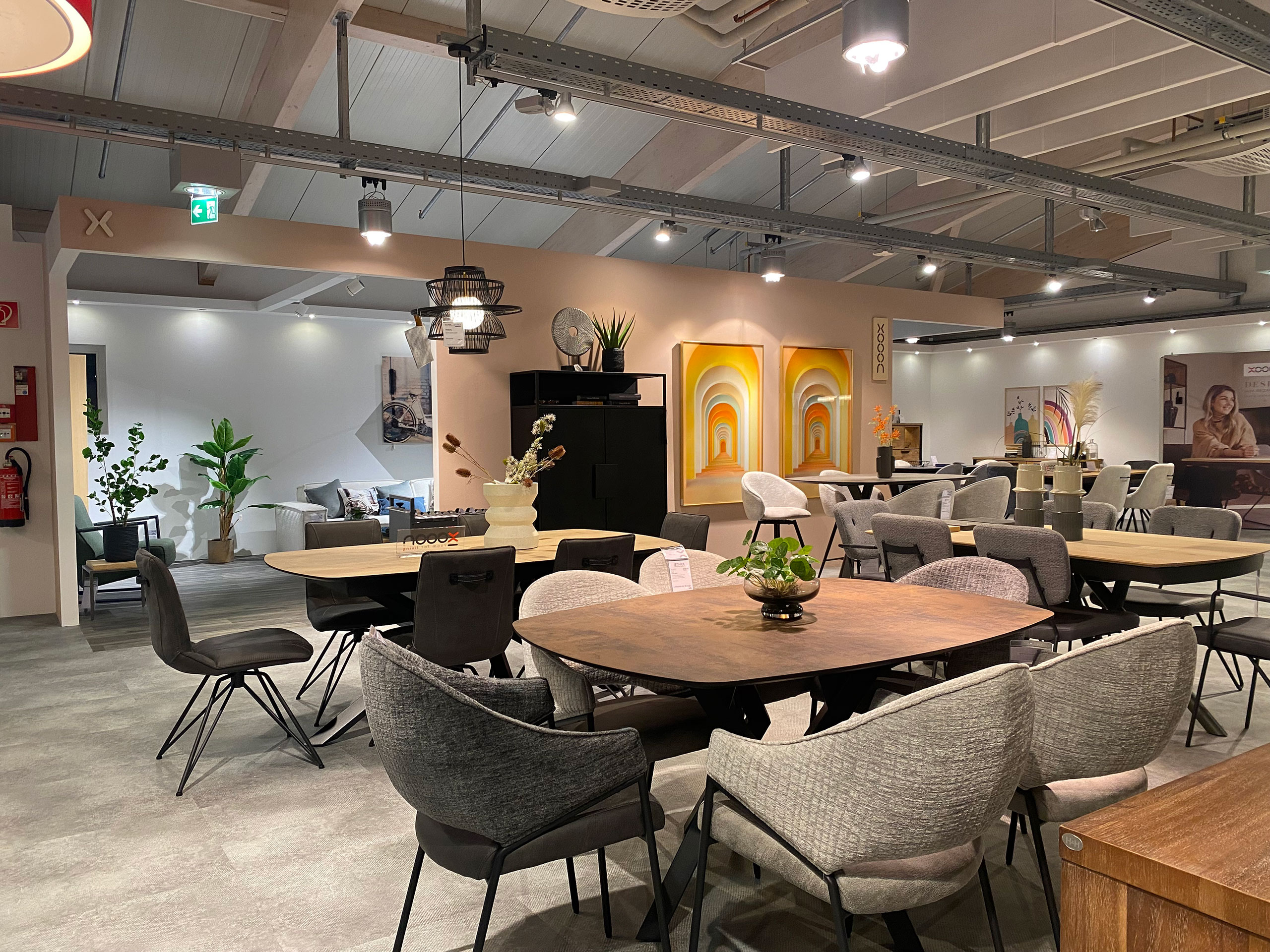 Moderner Möbel-Showroom mit verschiedenen Esstischen, Stühlen, Pflanzen und Wandkunst unter hellen Deckenleuchten.