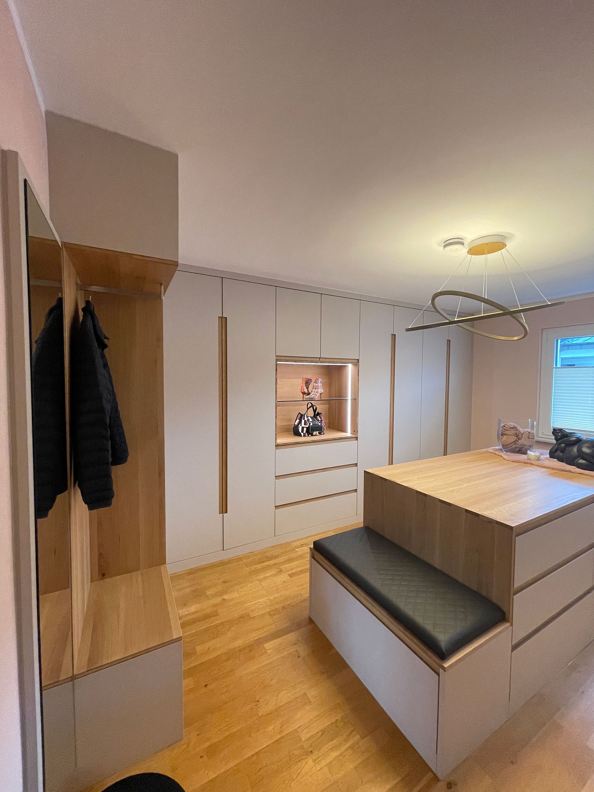 Moderner begehbarer Kleiderschrank mit Einbauschränken, einer gepolsterten Bank, Holzakzenten und einer modernen Leuchte.