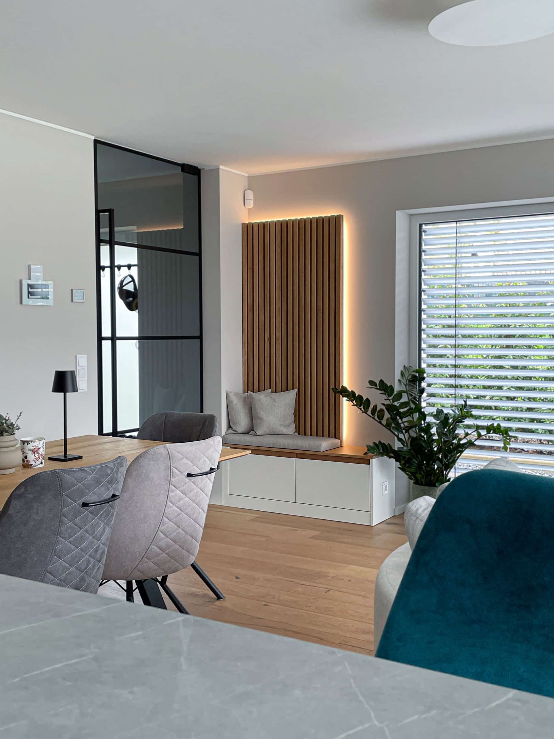 Moderner Wohnraum mit Fensterbank, Holzvertäfelung, Zimmerpflanze und grauen Esszimmerstühlen neben einem Tisch.
