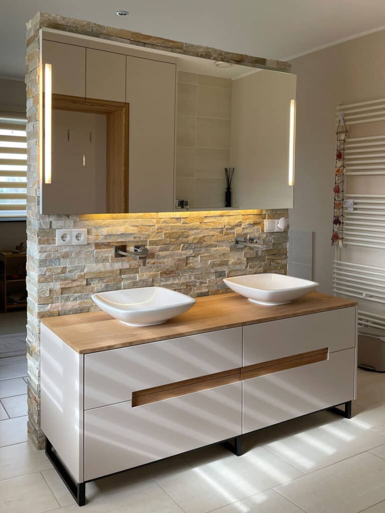Modernes Badezimmer mit Doppelwaschbecken, Akzentwand aus Stein, großem Spiegel und warmer Beleuchtung.