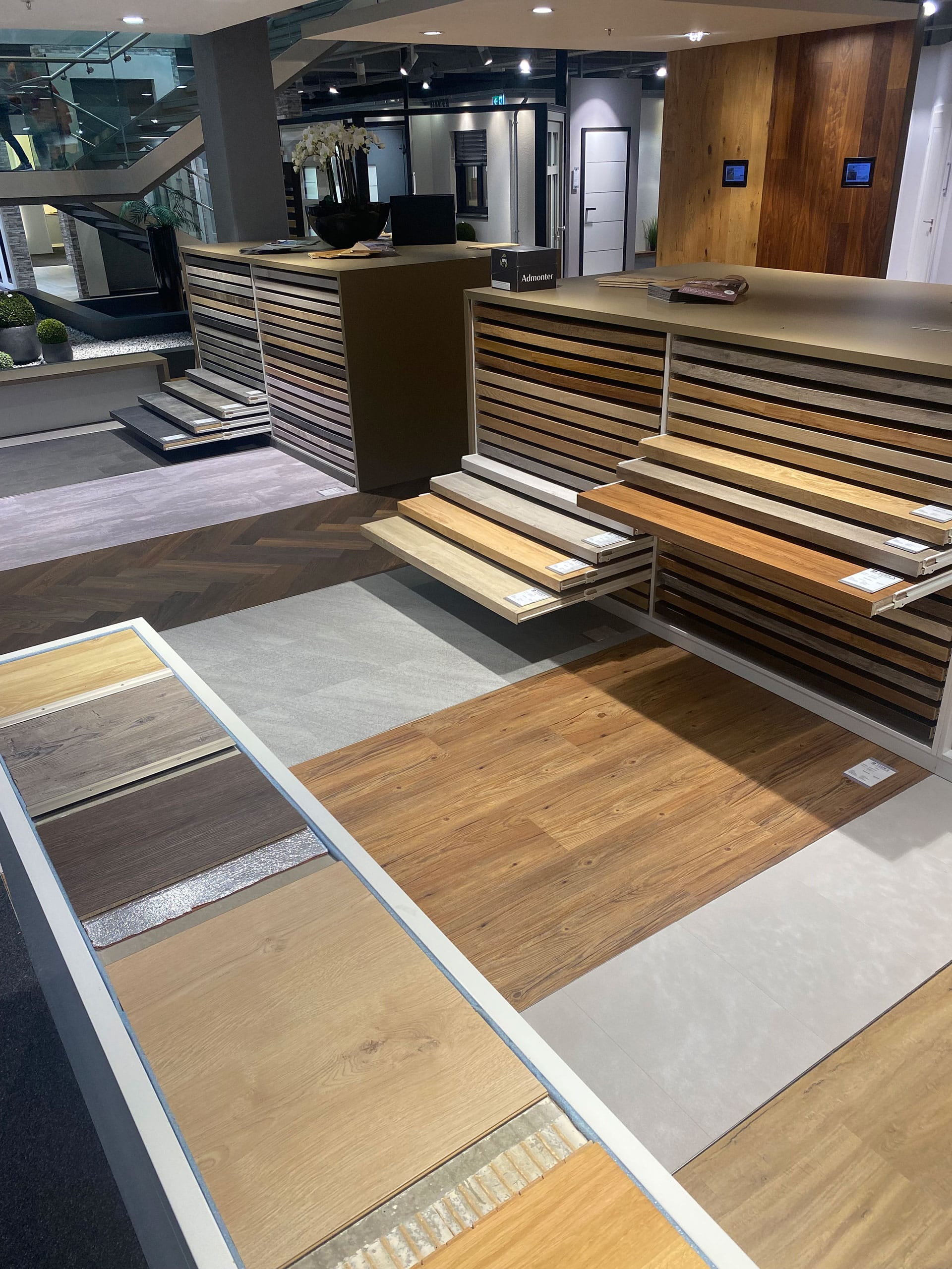 Ausstellungsraum mit verschiedenen Holz- und Laminatfußbodenmustern, die auf Regalen und Plattformen unter heller Beleuchtung angeordnet sind.