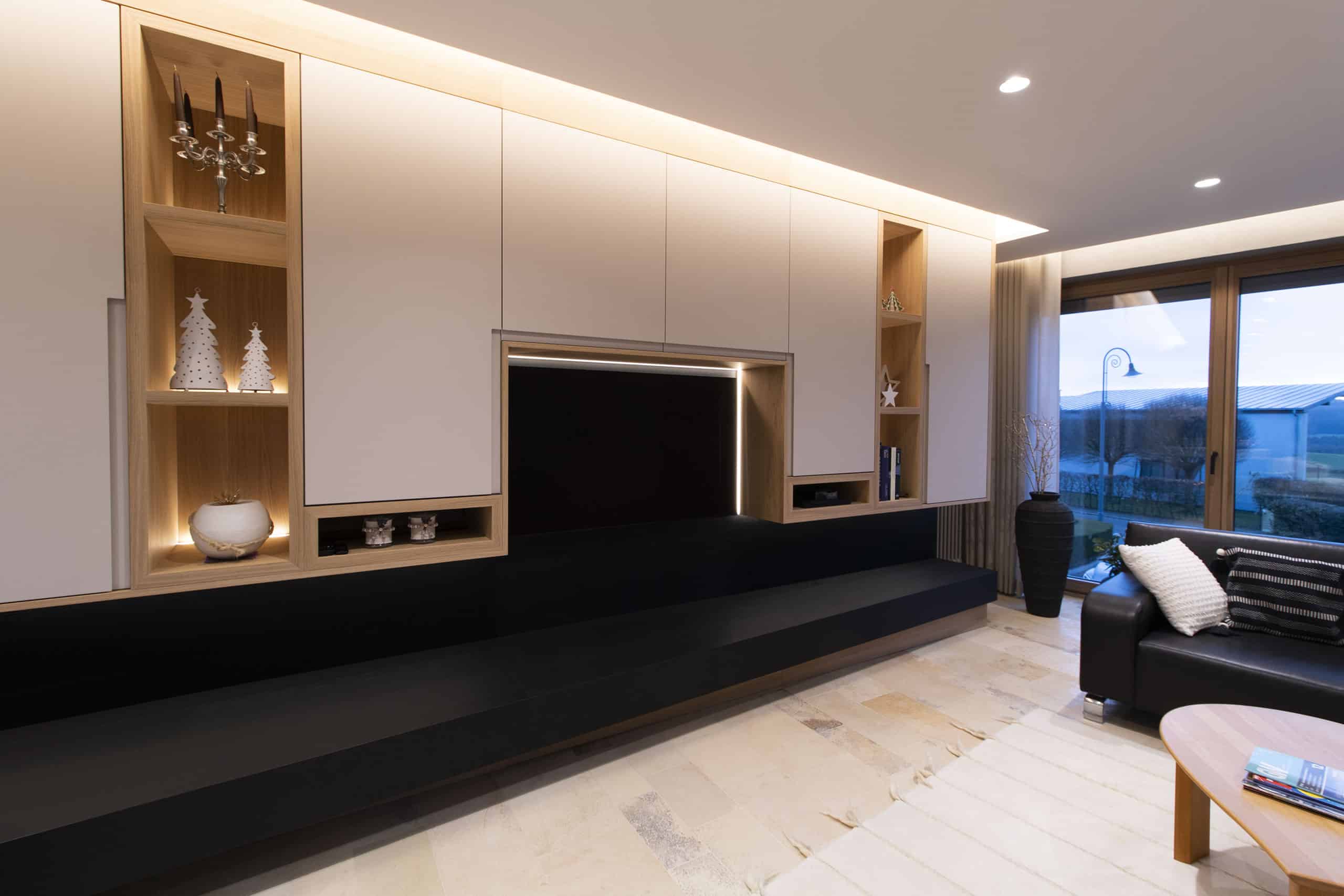 Modernes Wohnzimmer mit Einbauschränken, schwarzer Bank, neutralen Tönen und großem Fenster mit Blick nach draußen.